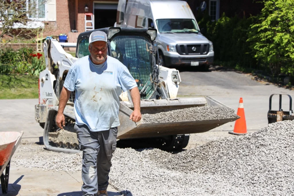 Destination Pools worker operating Bobcat skid steer to move gravel and aggregate during pool installation