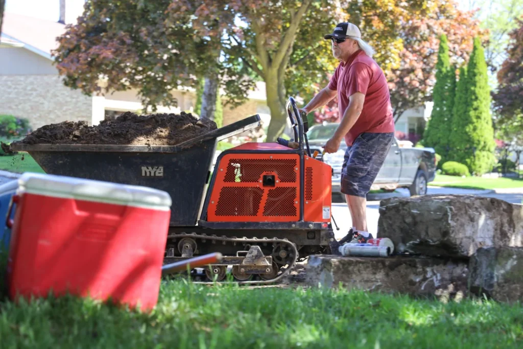 Worker operating Dingo compact track loader dumping soil during pool construction and landscaping project